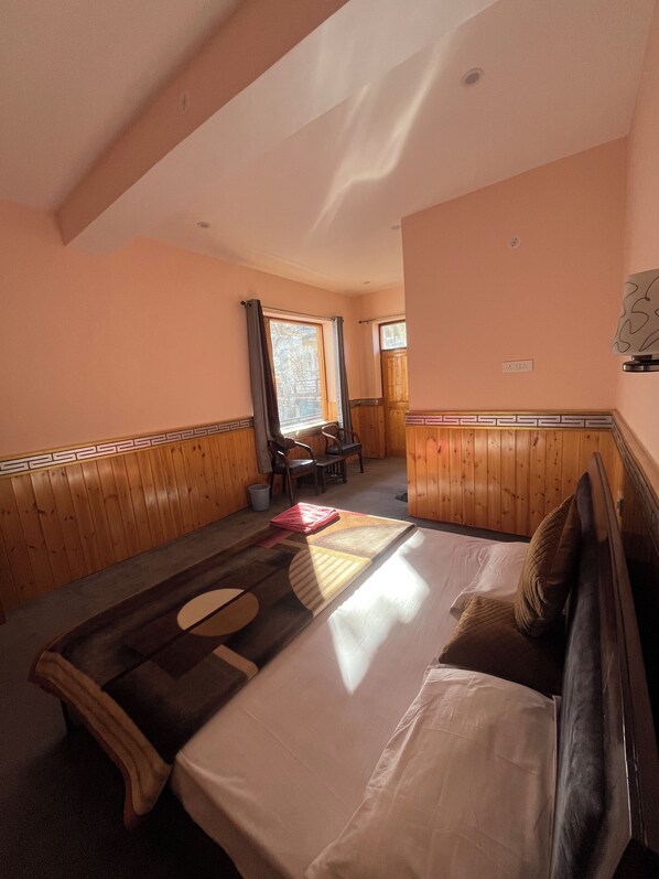 A bedroom with a bed, a wooden floor, a window, and a chair.
