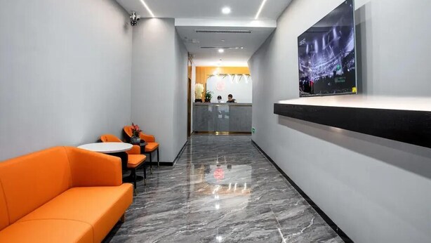 Een moderne hotellobby met een receptiebalie, een zithoek met oranje banken en een grote flatscreen televisie aan de muur.