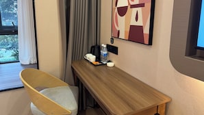Een hotelkamer met een houten bureau, een stoel, een koffiezetapparaat, waterflessen en een schilderij aan de muur.