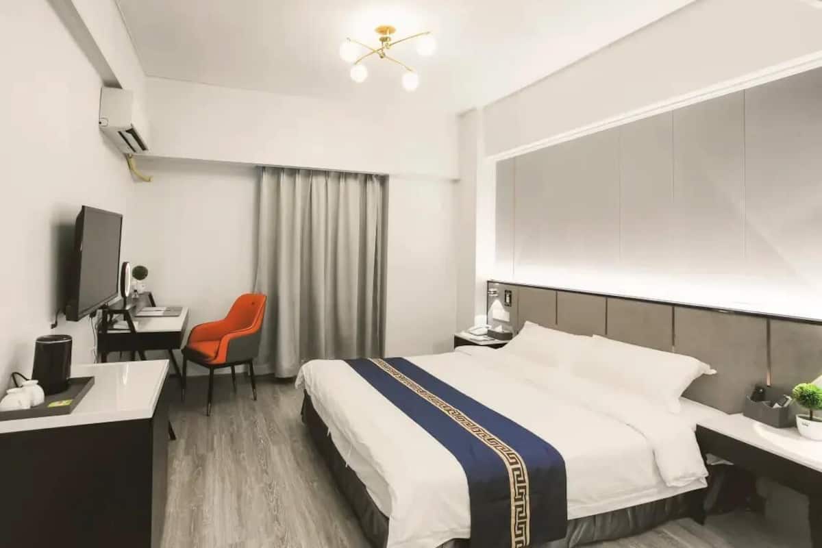 A modern hotel room with a bed, desk, chair, and a large window.