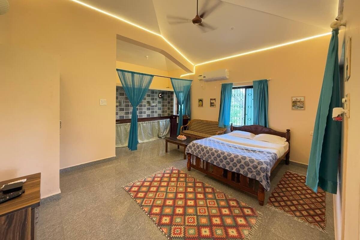 A bedroom with a bed, a ceiling fan, a window with curtains, a wall-mounted air conditioner, and a patterned rug.