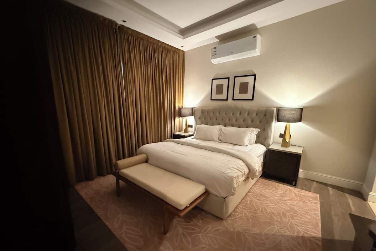 Ein Hotelzimmer mit einem großen Bett, einer Bank, einem Nachttisch mit Lampe und einer Klimaanlage an der Wand.
