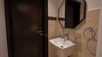 A bathroom with a dark wooden door, a white sink, a glass shelf above the sink, a mirror, and a towel ring.
