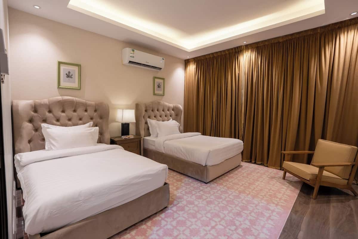 Ein Hotelzimmer mit zwei Betten, einem Sessel, einem Nachttisch, einer Klimaanlage und einem großen Fenster mit Vorhängen.
