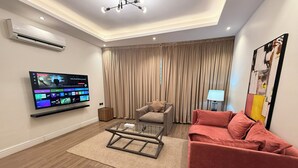Een moderne woonkamer met een flatscreen televisie, een glazen salontafel, een rode bank en een beige gordijn.
