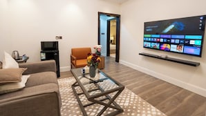 Een moderne woonkamer met een flatscreen televisie aan de muur, een bank, een salontafel en een kleine tv-kast met een waterkoker.