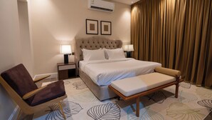 Een hotelkamer met een bed, twee bedlampen, een stoel, een bank en een groot raam met gordijnen.