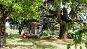 A rustic wooden playhouse with a slide, surrounded by large trees and a grassy yard. - Le vieux four self-catering cottage in the countryside (Corbarieu)