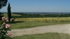 A rural landscape with a gravel path, green fields, and a distant view of a town. - Le vieux four self-catering cottage in the countryside (Corbarieu)