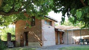 A brick building with a tiled roof, a gravel driveway, and a covered outdoor seating area with chairs. - Le vieux four self-catering cottage in the countryside (Corbarieu)