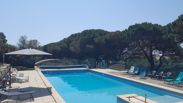 A rectangular swimming pool with a clear blue water surface, surrounded by a tiled deck. There are lounge chairs and a large umbrella providing shade. - Le vieux four self-catering cottage in the countryside (Corbarieu)