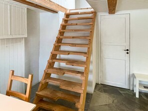 Una escala de fusta en una habitació amb una porta blanca i una cadira.