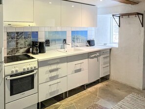 Een moderne keuken met witte kastjes, een Bosch oven, een koffiezetapparaat en een raam dat voor natuurlijk licht zorgt.
