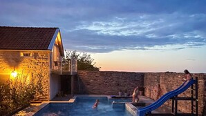 A swimming pool with a slide, a stone wall, and a building with a tiled roof. - 4 Person Holiday Home in Morbylanga (Morbylanga)