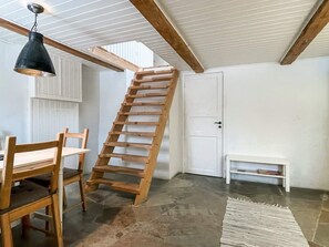 Een kamer met een houten ladder, een witte deur, een bank en een eethoek met stoelen en een tafel.
