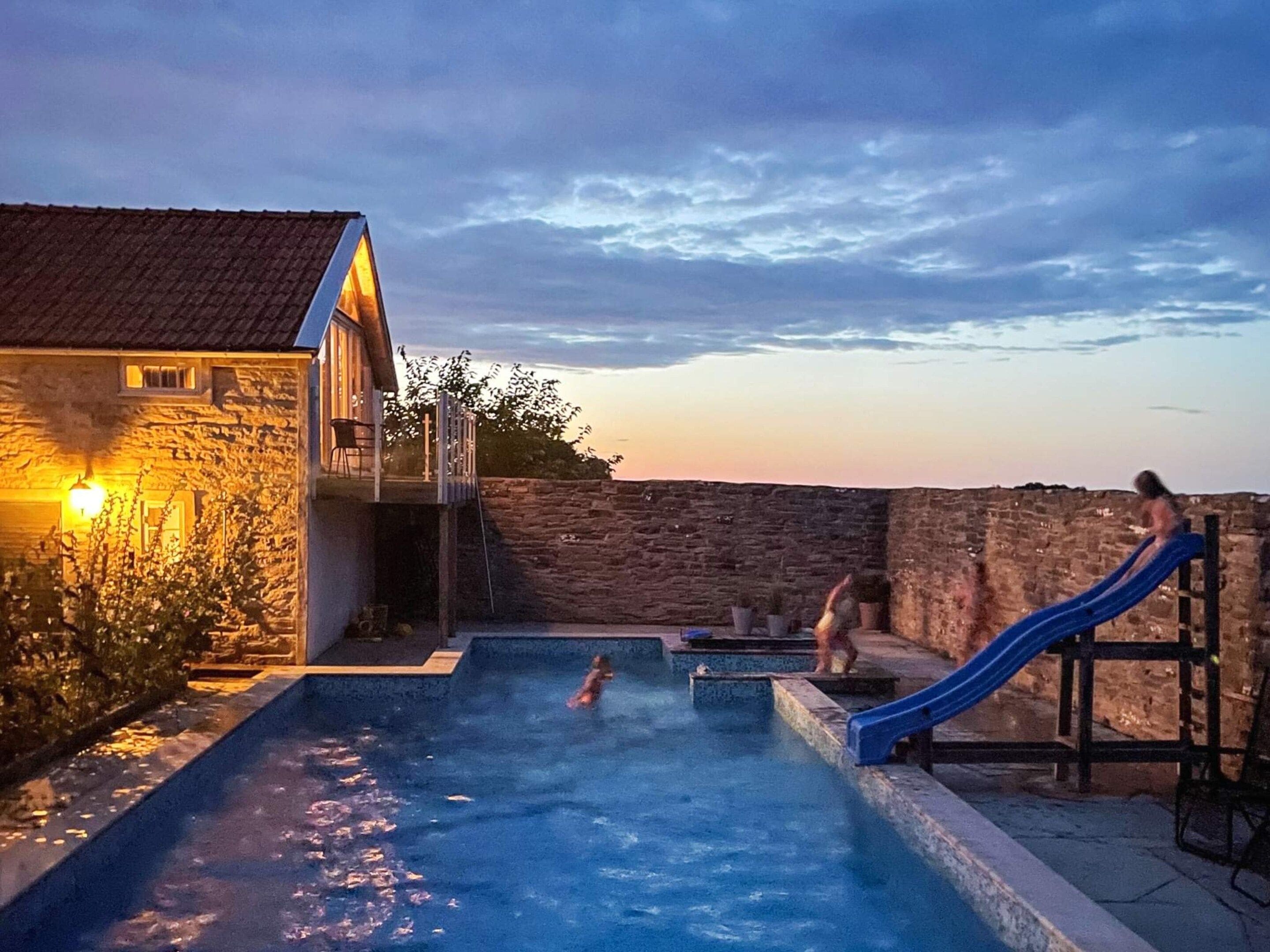 En swimmingpool med en rutsjebane, en stenvæg og en bygning med et tagtækket tag.