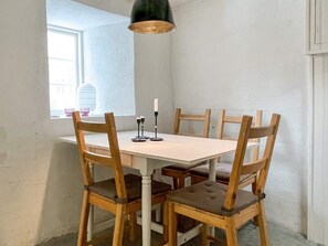 Een eettafel met zes houten stoelen, een hangende hanglamp en een raam met uitzicht op gebouwen.