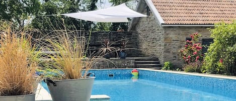 Una piscina con muelle de madera, rodeada de plantas en macetas y un muro de piedra.