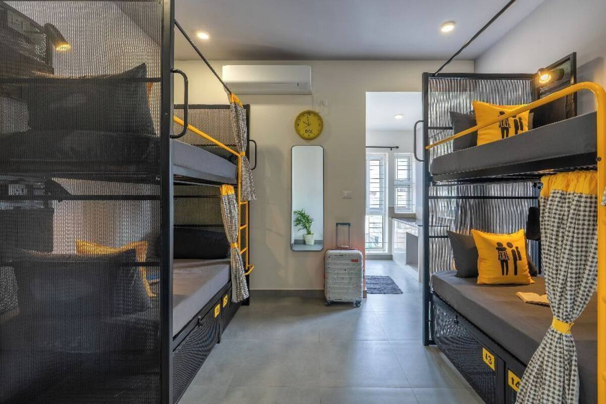 A dormitory-style room with bunk beds, a clock, a mirror, and a suitcase.