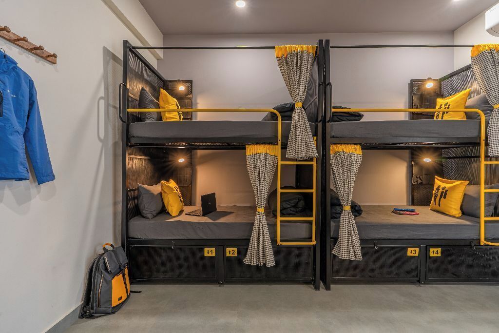 A bunk bed room with two levels, each with a mattress and pillows. There is a backpack on the floor.