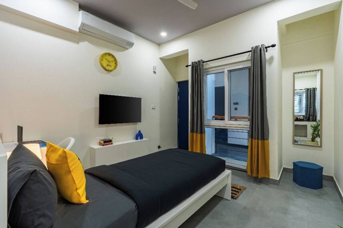 A modern bedroom with a bed, a flat-screen TV, a clock, and a window with curtains.