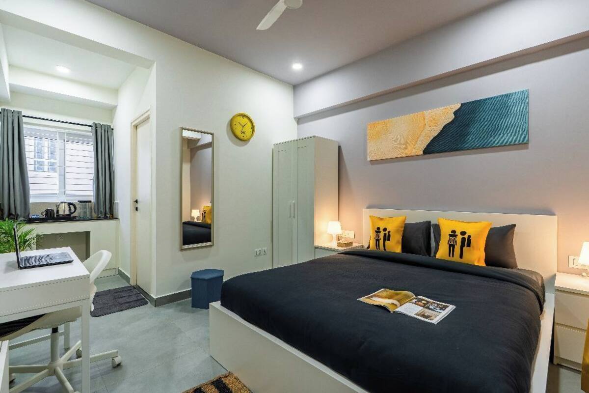 A modern bedroom with a bed, a desk, a wardrobe, and a clock on the wall.