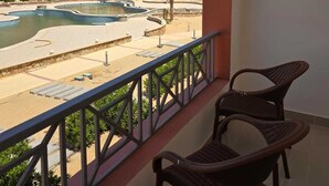 Un balcon offrant une vue sur une piscine et une plage, avec un hôtel à plusieurs étages et doté de nombreux balcons en contrebas.