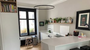 A modern kitchen with a large island, black bar stools, a window with black curtains, and a bookshelf filled with books. - House Nantes center in private cul-de-sac (Nantes)