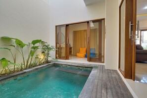 Ein moderner Poolbereich im Innenbereich mit Holzboden, Schiebegläsern zu einem Wohnraum und verschiedenen Pflanzen.