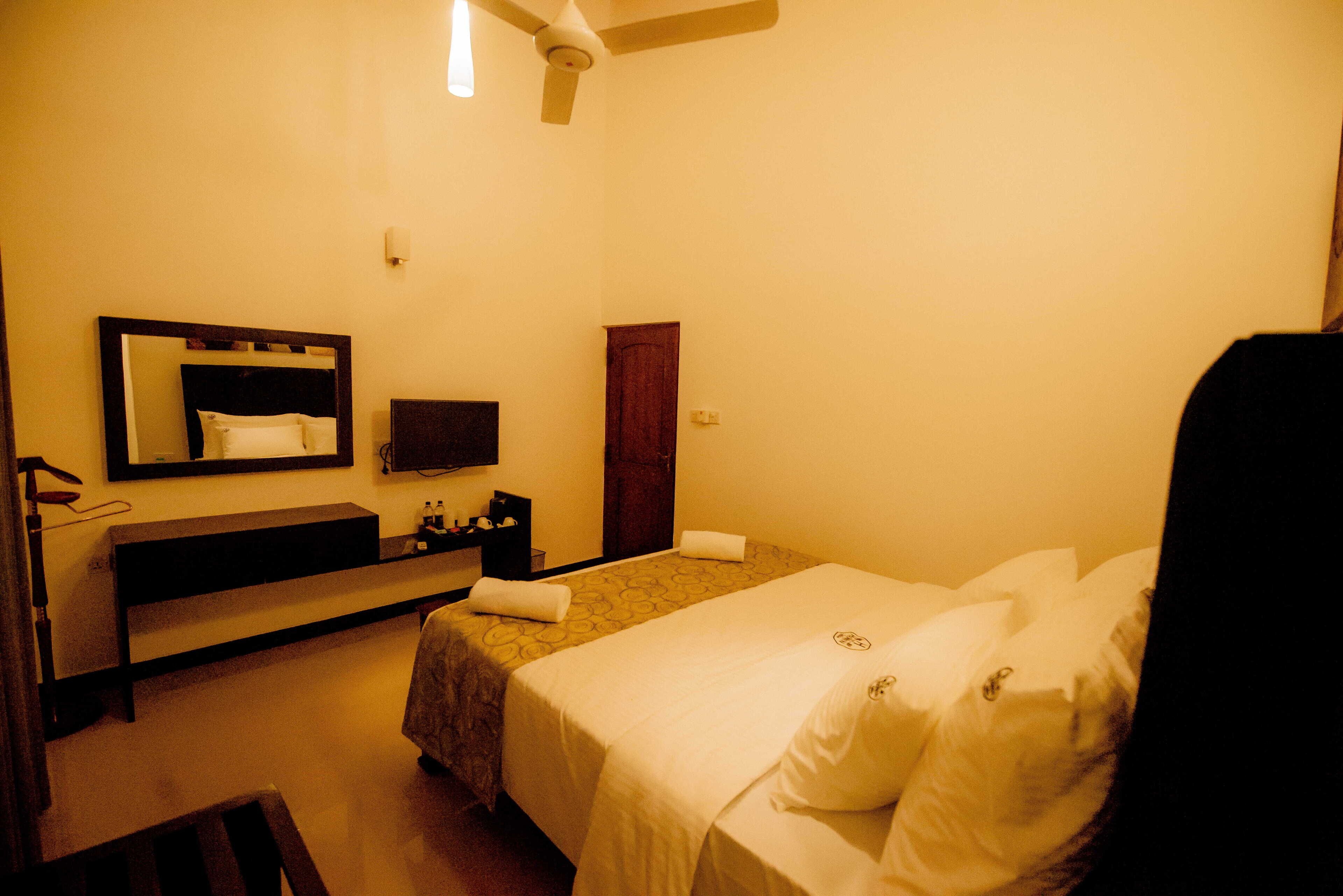 A hotel room with a bed, a bedside table, a mirror, a TV, and a ceiling fan.