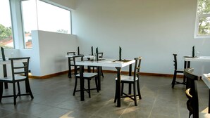 Ein Essbereich mit weißem Tisch, schwarzen Stühlen, großen Fenstern und Fliesenboden.