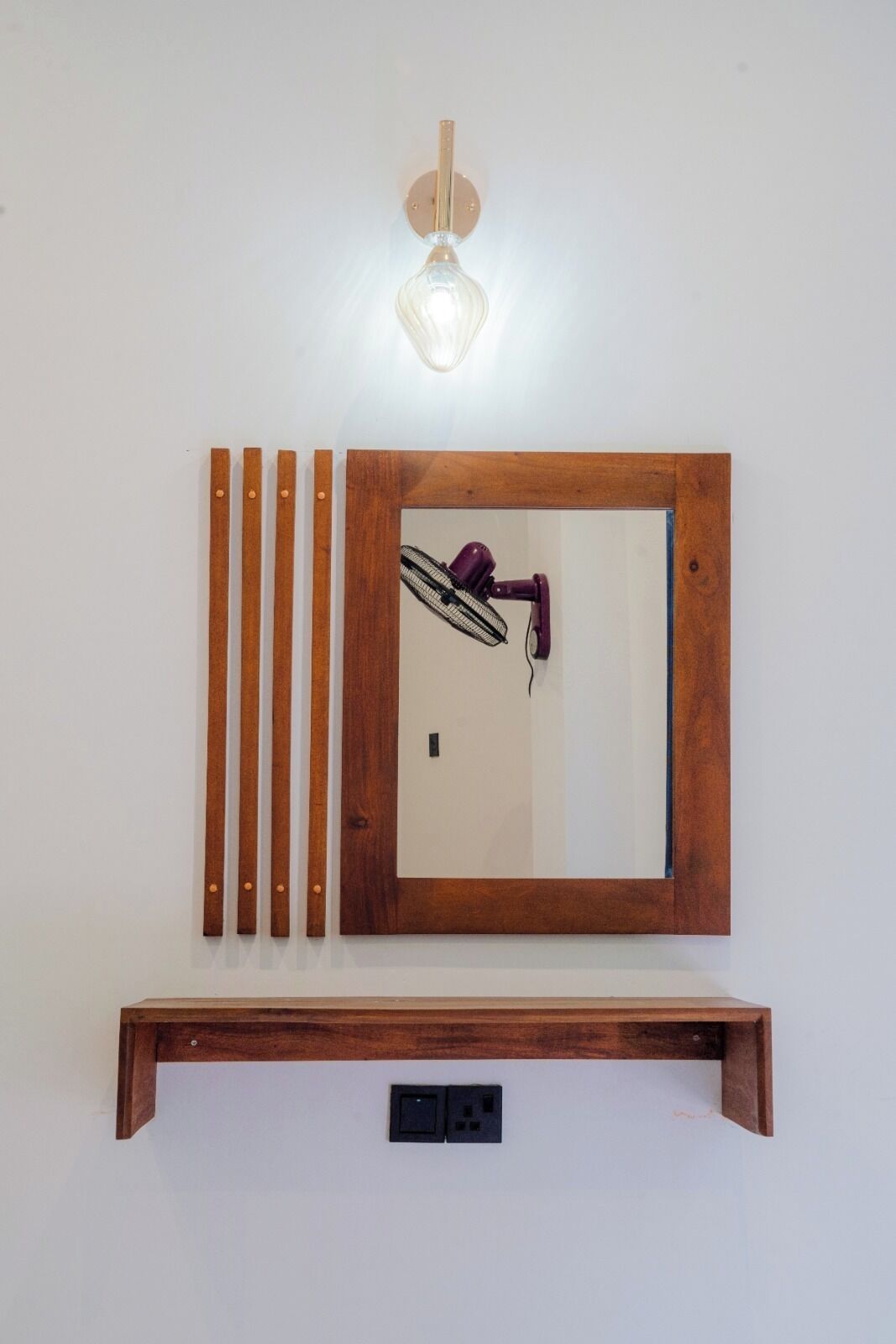 A wall-mounted wooden shelf with a mirror, a purple fan, and a light fixture.