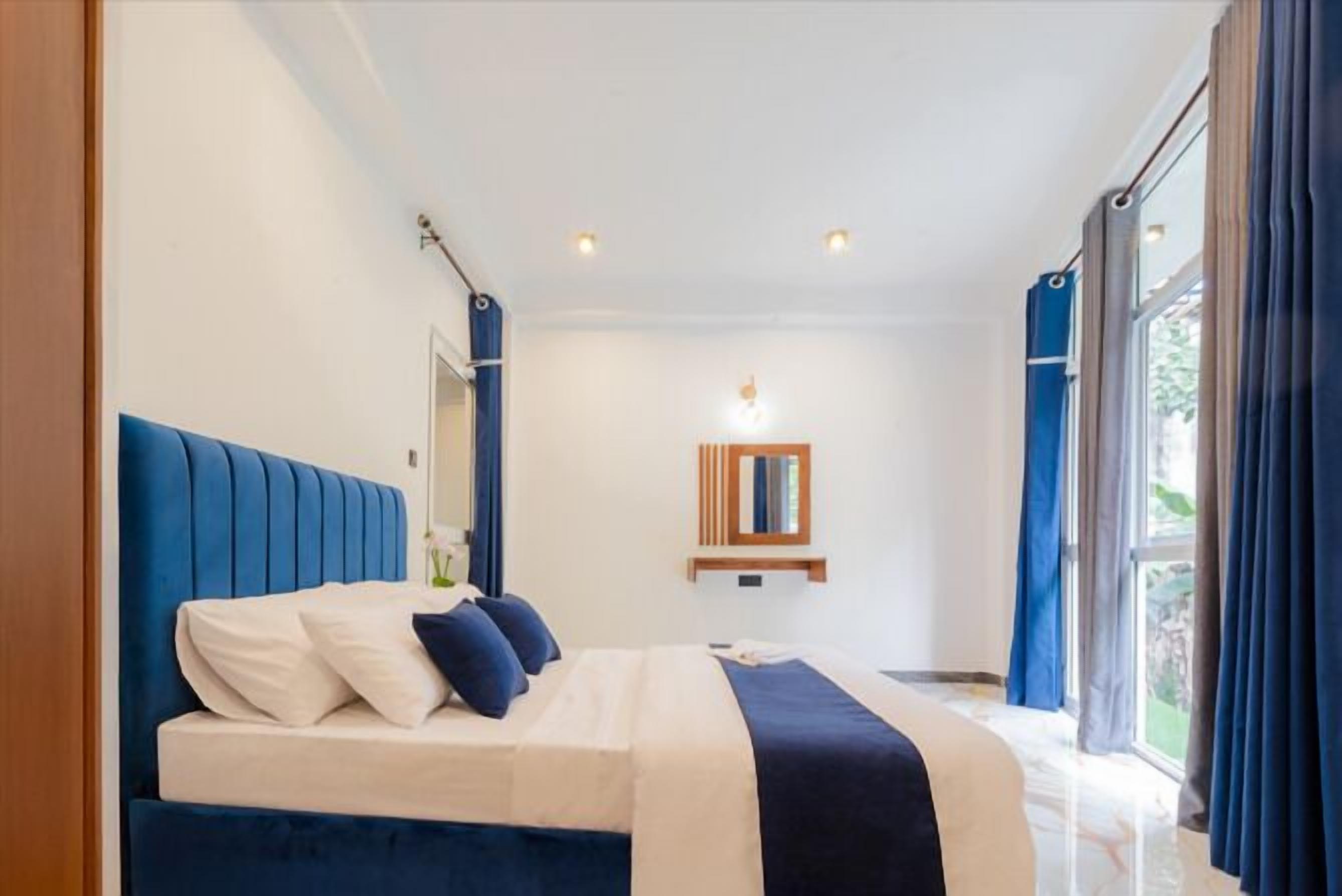Een moderne slaapkamer met een groot bed, nachtkastje, spiegel en raam met gordijnen.