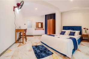 Una camera da letto con un letto, una scrivania, una sedia, uno specchio e una ventola a parete.