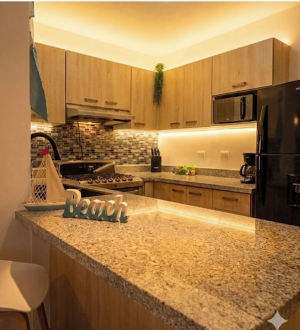 Una cocina moderna con encimeras de granito, armarios de madera, estufa de acero inoxidable y refrigerador negro.