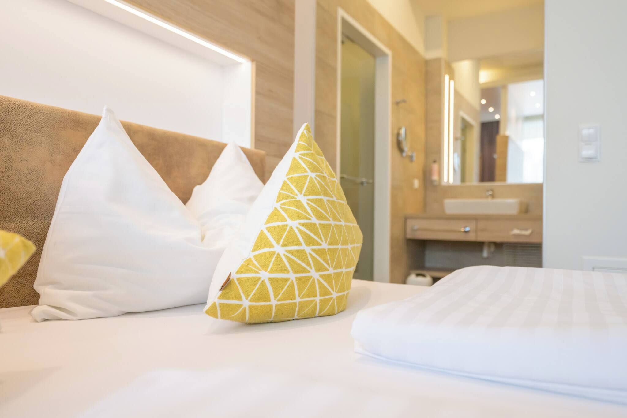 A hotel room with a bed, white pillows, and a wooden headboard.