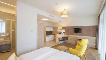 Una habitación de hotel con cama, escritorio, silla, televisión y kitchenette.