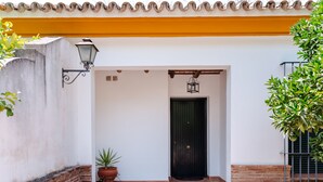 Entrada de un edificio con una puerta negra, una planta en maceta y una lámpara fijada a la pared.