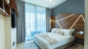A modern hotel room with a large bed, a wooden headboard with geometric lighting, a TV mounted on the wall, and a view of the city through large windows.