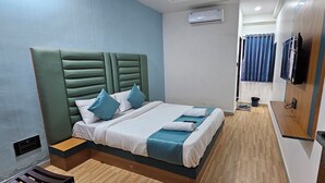A neatly arranged hotel room with a bed, a small table, a TV, and a shower area. - Hotel Jalsa (Surat)