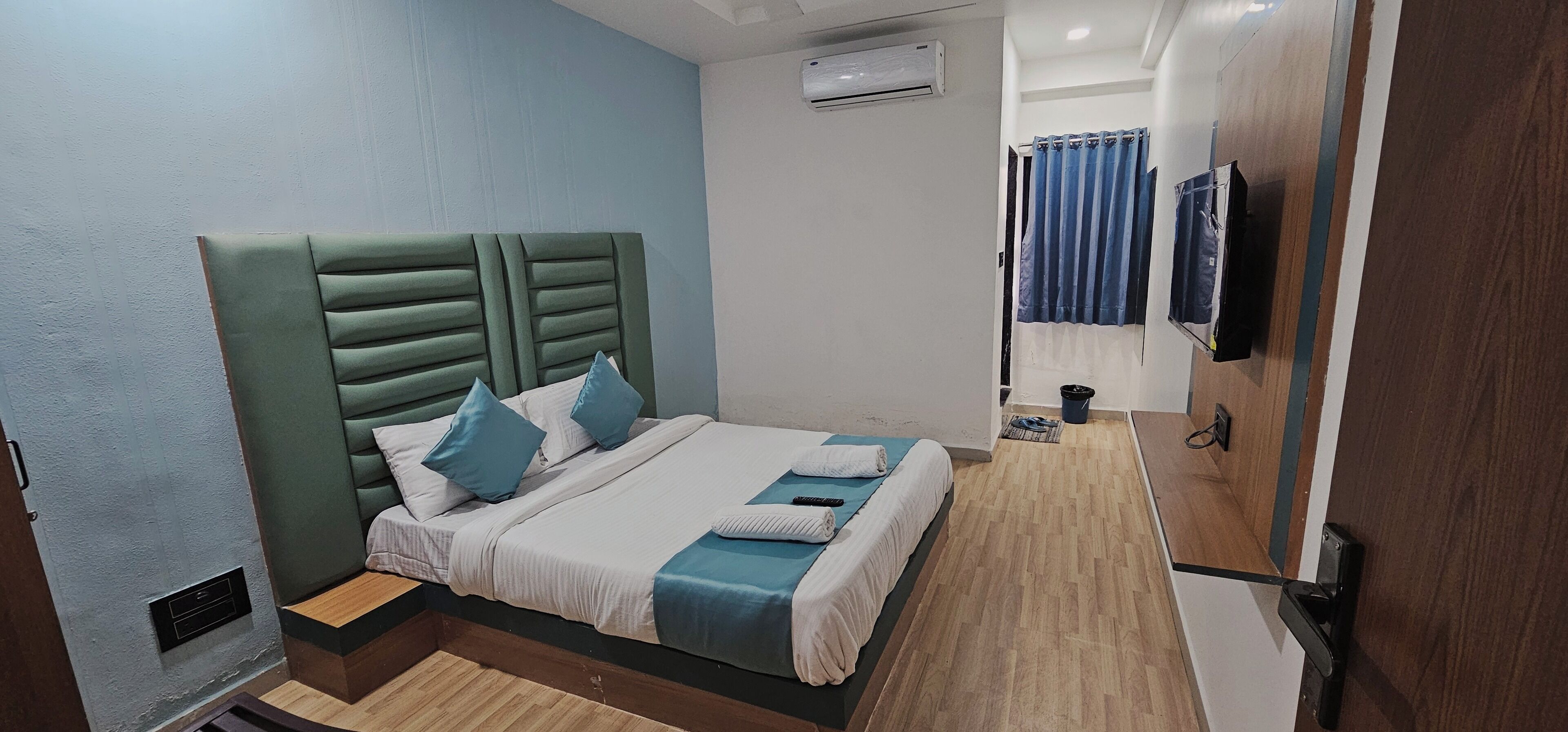 A neatly made bed with a green headboard, a small bedside table, and a wall-mounted TV.
