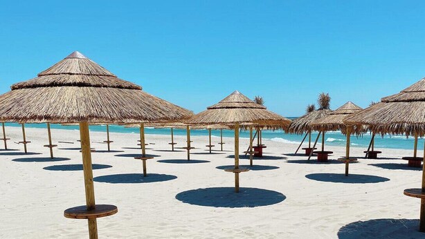 A beach with thatched umbrellas and wooden stools. - Roomsalentopalace (Torre San Giovanni)