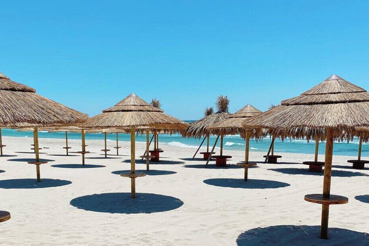 A beach with thatched umbrellas and wooden stools.