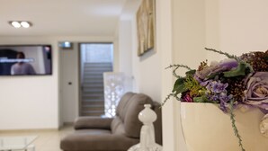 A living room with a sofa, a TV, and a decorative vase with flowers. - Roomsalentopalace (Torre San Giovanni)