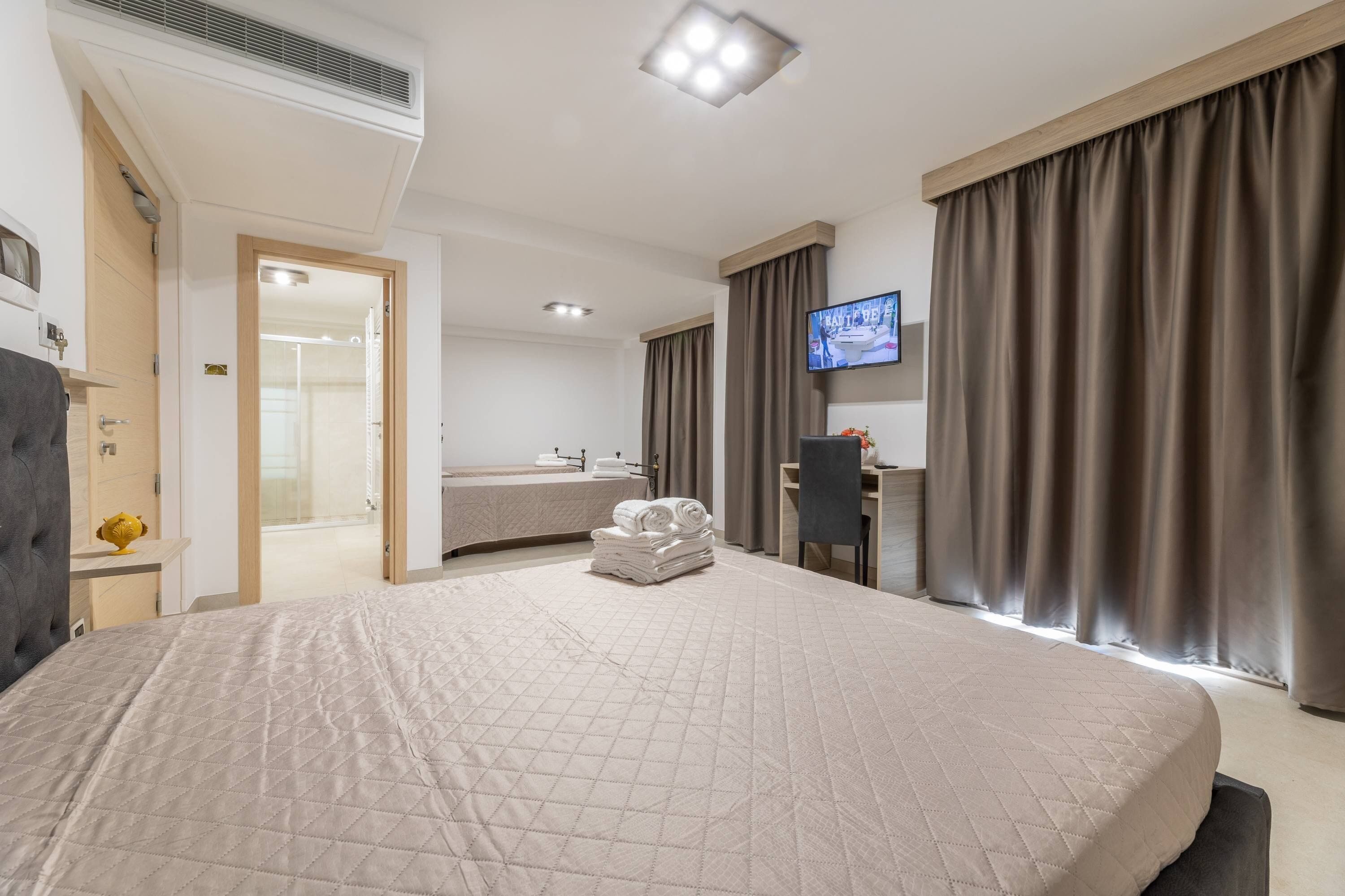 A hotel room with a large bed, a desk, a television, and a bathroom visible through an open door.