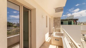 A balcony with a sliding glass door, a small outdoor seating area, and a view of neighboring buildings. - Roomsalentopalace (Torre San Giovanni)