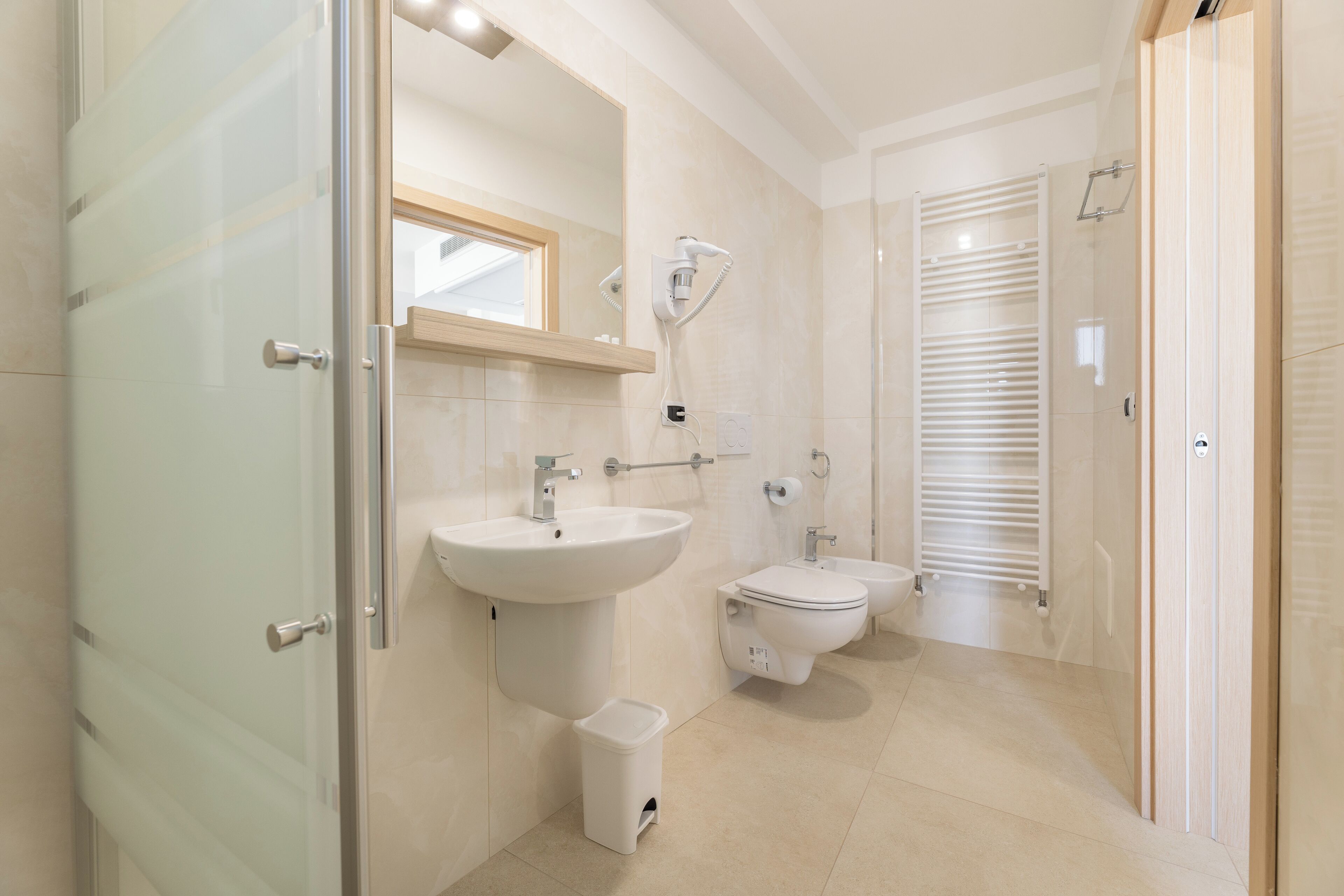 Un baño moderno con cabina de ducha de vidrio, lavamanos pedestal, inodoro y bidé.