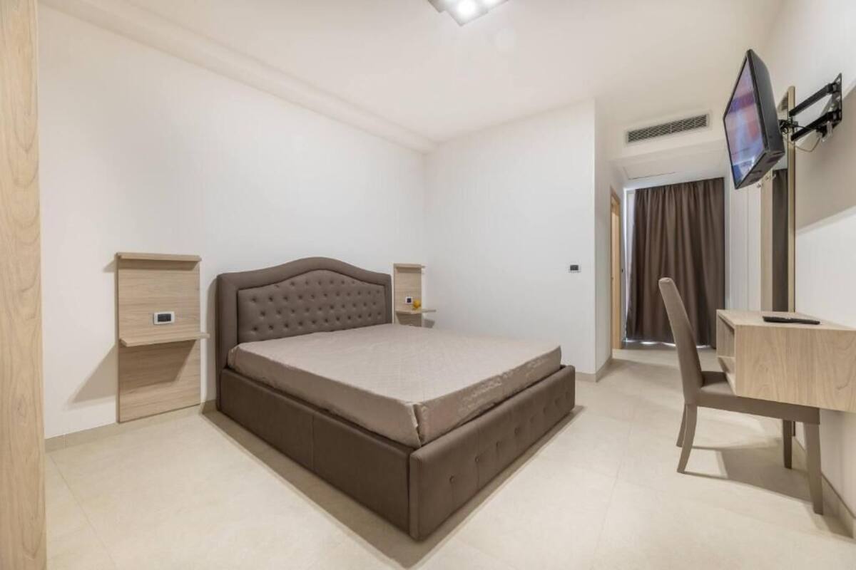 A bedroom with a bed, bedside tables, a desk, and a TV.