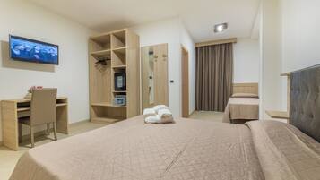 Habitación de hotel con cama, escritorio, silla, armario, televisor y espejo.