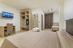 Habitación de hotel con cama, escritorio, silla, armario, televisor y espejo.